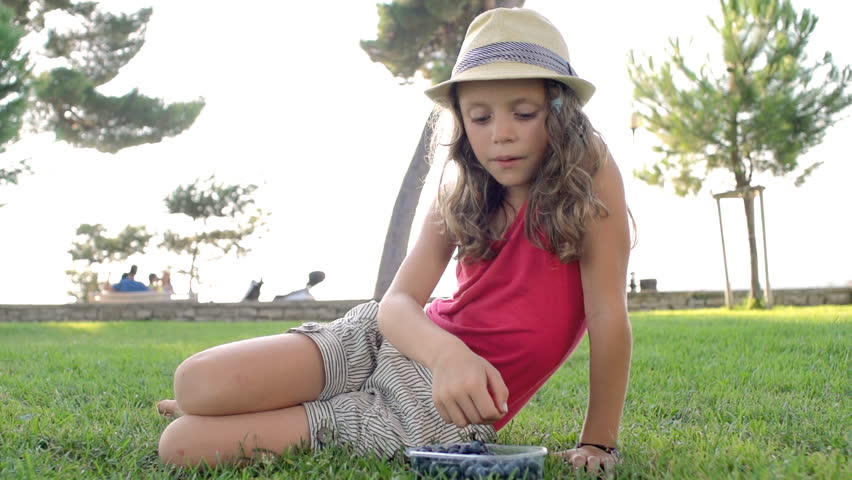 Slow Motion Shot Of A Cute Little Girl Eating Blueberries Out In The Park