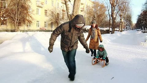 Father, who is pulling his son in sled. Park in winter.
