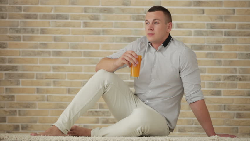 Handsome guy sitting on floor drinking juice and smiling