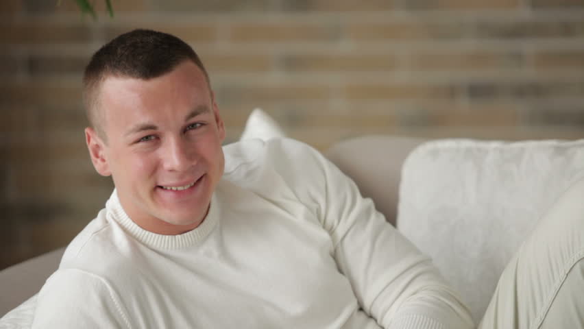 Good-looking guy relaxing on couch using touchpad and smiling at camera