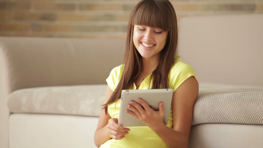 Cute girl sitting on floor using touchpad and smiling at camera