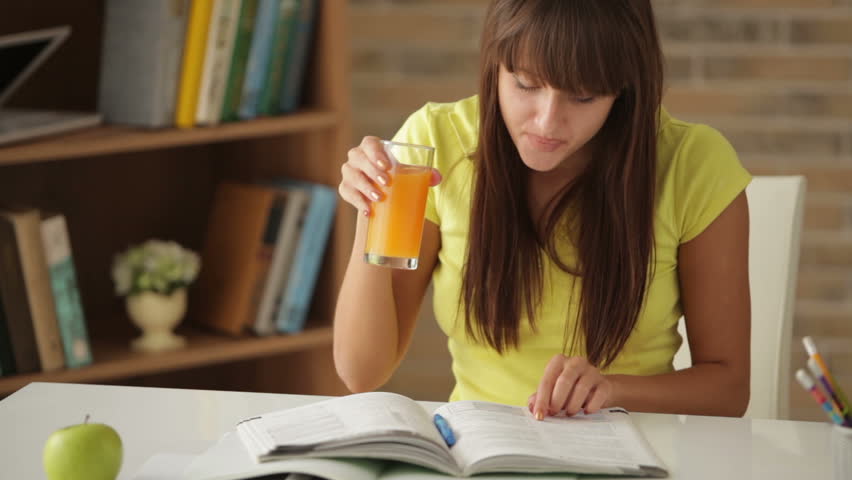 Female college student sitting at table writing in notebook and drinking juice