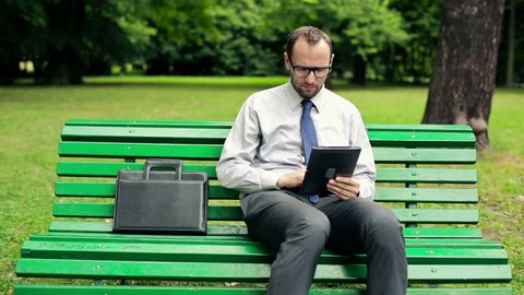 Happy businessman with tablet computer in the park

