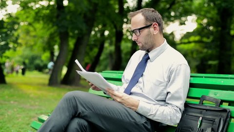 Tired, overworked businessman with documents in the park
