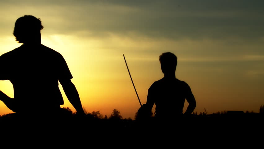 Men at sunset fighting with swords