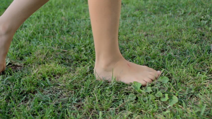 Slow Motion Shot Of A Girl's Bare Feet Walking Over Green Grass Field