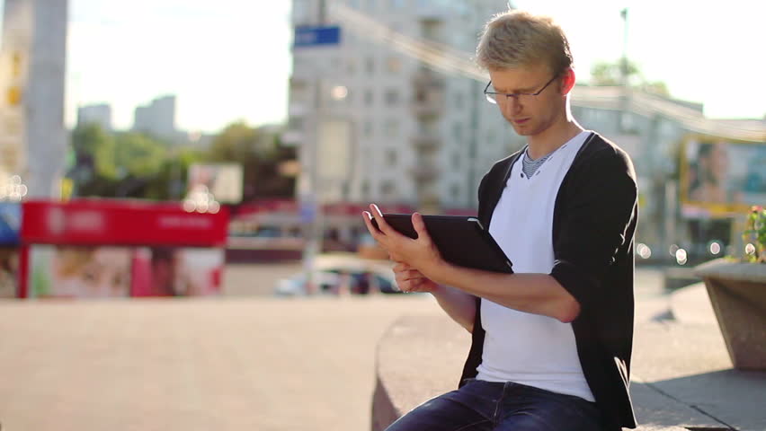 Incoming phone call, man sits on city square reads tablet device