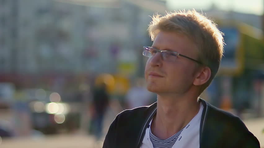 Smiling young man takes off glasses looking at camera city scape