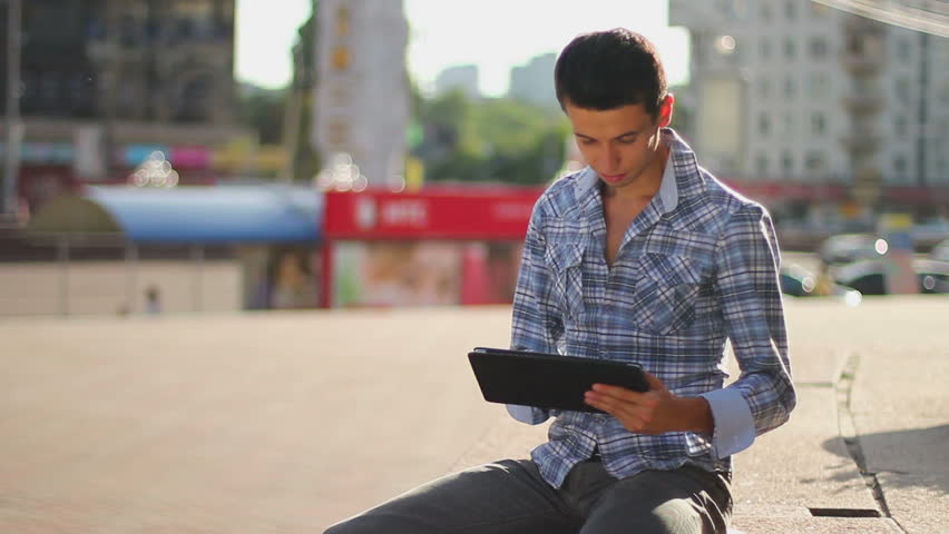 Young man sitting on square reading touch pad computer inspiring