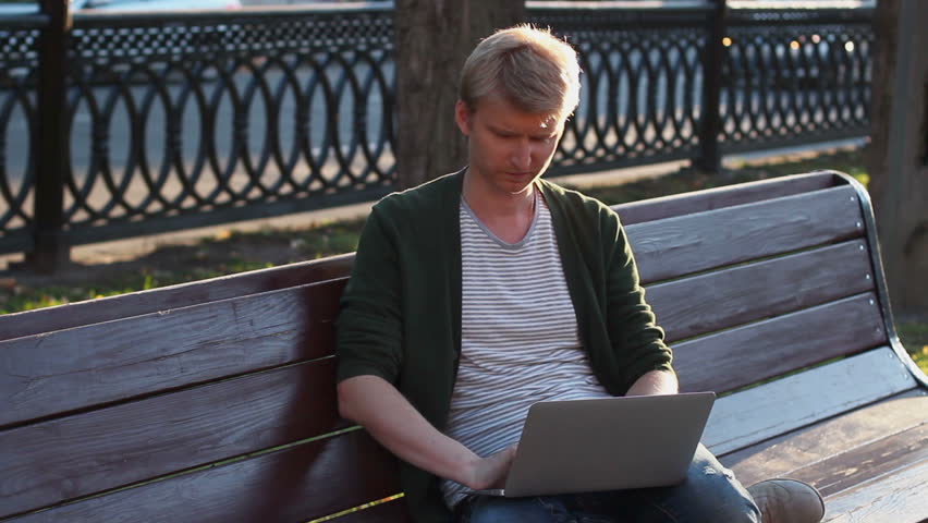 Man in park working laptop reading and writing messages browsing