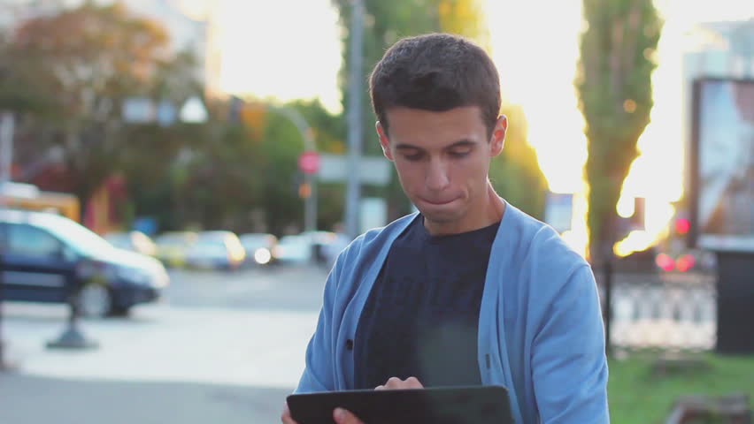 Young adult male browsing tablet pc computer, looking at camera