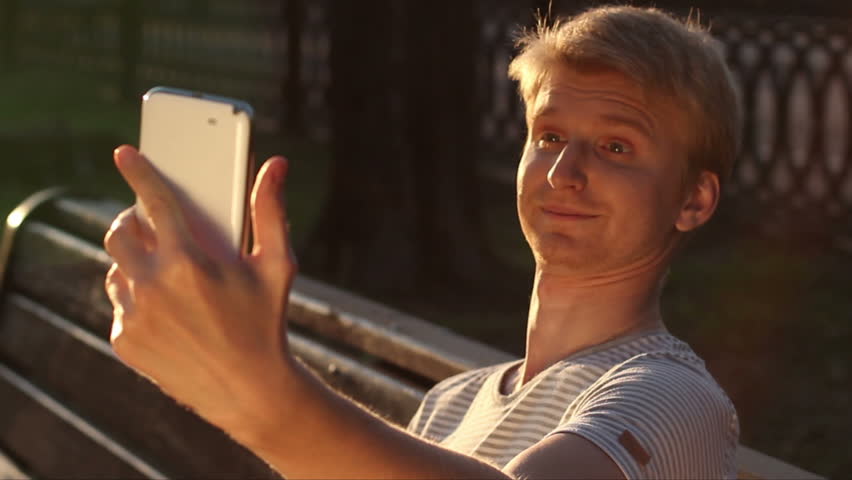Funny blond man taking photo himself in park for social networks