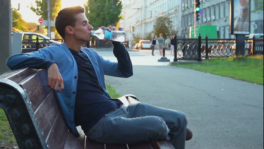 Young adult male sitting in park enjoying life drinking water