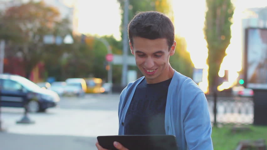 Young male browsing tablet pc computer smiling at camera outdoor