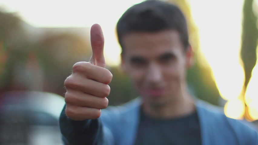 Young man thumb up right hand rack focus, daytime outdoors park