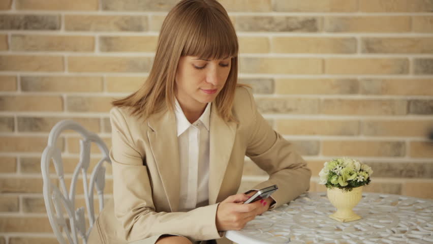 Cheerful young woman sitting at cafe and using mobile phone
