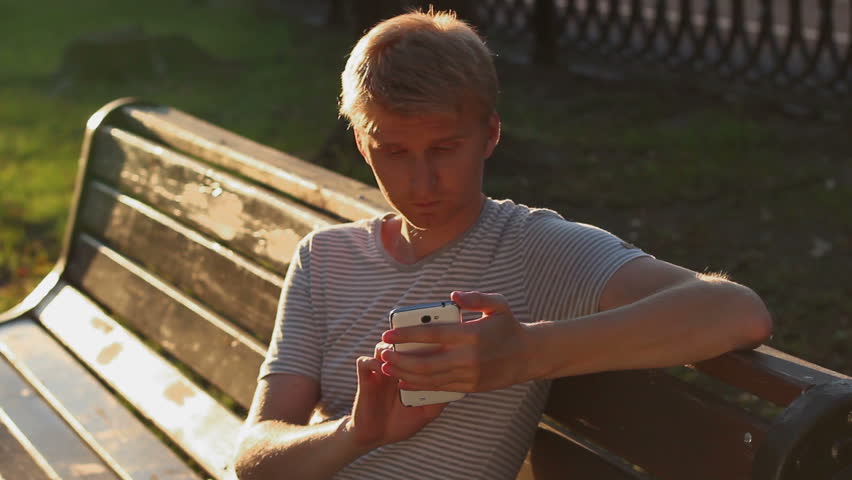 Blond male writing sms message to girlfriend sitting in park