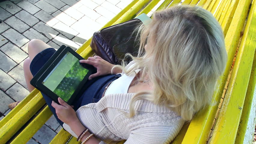 Young woman sets aside tablet pc sitting on yellow bench park