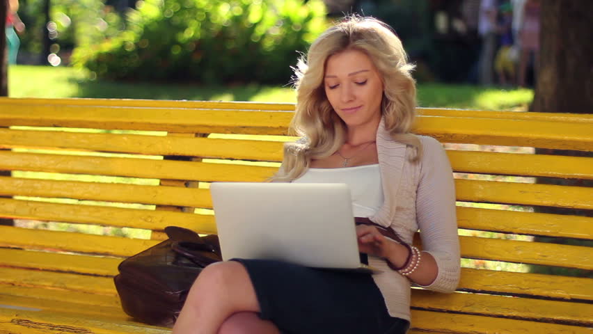 Businesswoman in park typing message to laptop smiling