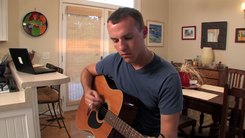 A young man plays the guitar.  Dolly shot.