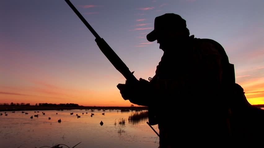 Duck hunter loading gun at sunrise.