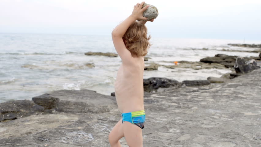 Slow Motion Shot Of A Little Red-Haired Boy Throwing A Stone Into The Sea. 