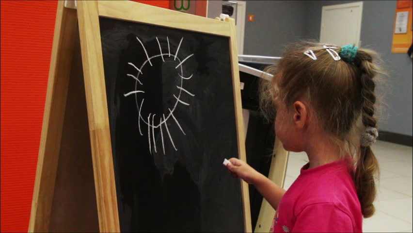 little girl drawing sun with chalk on blackboard