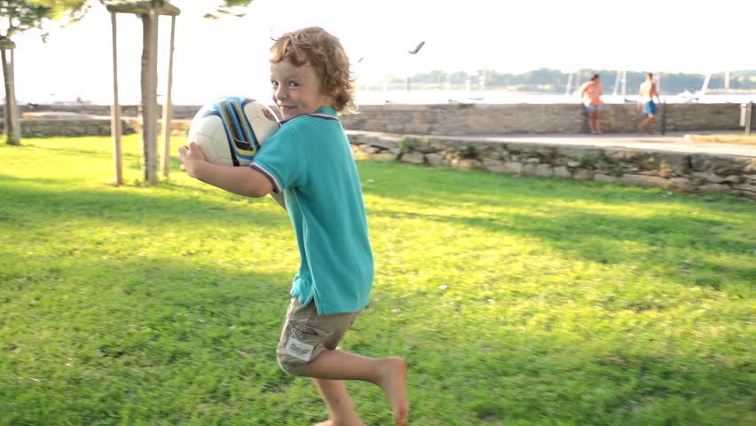 Slow Motion Shot Of A Cute Red-Haired Boy Holding A Ball, Running Away Over