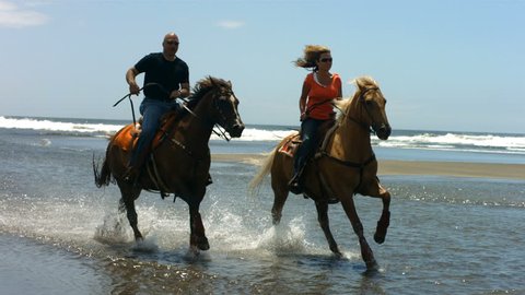 Couple riding horses on beach, slow motion