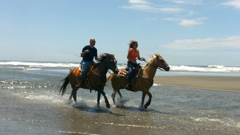 Couple horseback riding on beach, slow motion