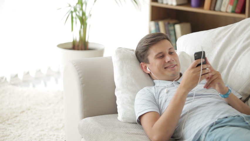 Good-looking guy lying on sofa listening to music with headphones and smiling