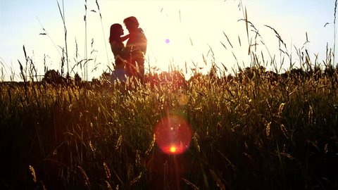 A silhouetted couple hug, kiss and then walk in a wide open golden field at sunset  Stock Video