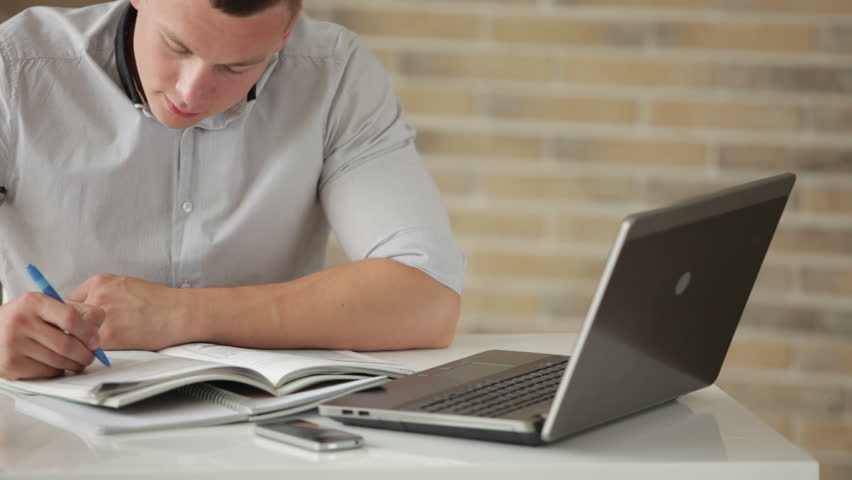 Young man sitting at table and studying with laptop