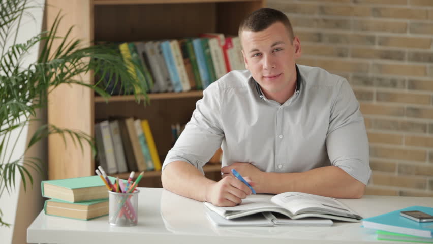 University student sitting at table surrounded by books and writing in notebook