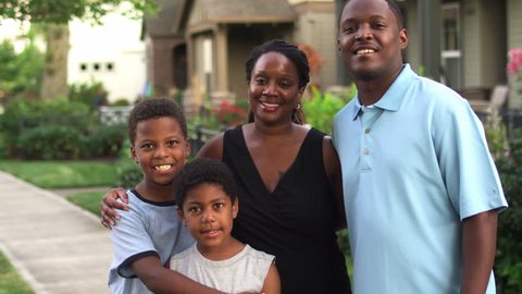 A cute African American family stands outside of a house and smiles for the camera. Medium shot วิดีโอสต็อก