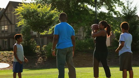 An African American family plays keep the ball away from their dad in a park. Wide shot