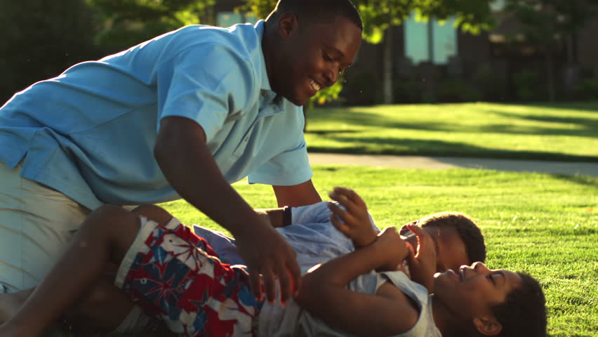 African American dad plays with his sons by tickling them. Medium shot