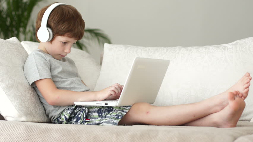 Little boy relaxing on sofa and using laptop