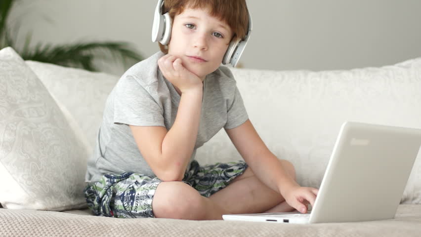 Funny boy in headset sitting on sofa and using laptop
