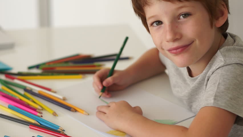 Little boy sitting at table and drawing with colored pencils