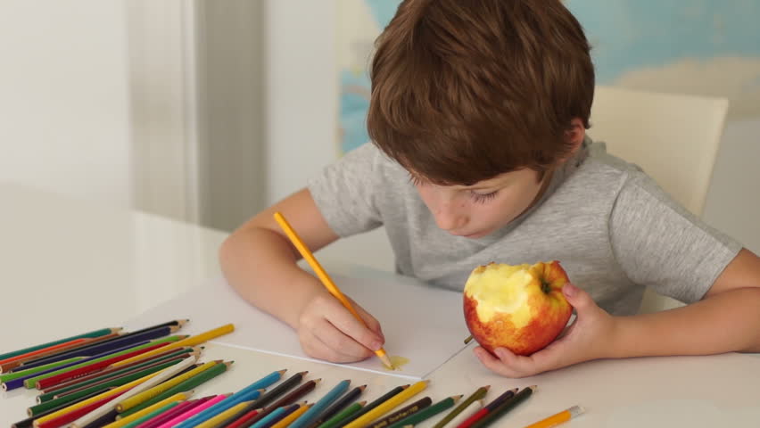 Funny little boy sitting at table and drawing with colored pencils