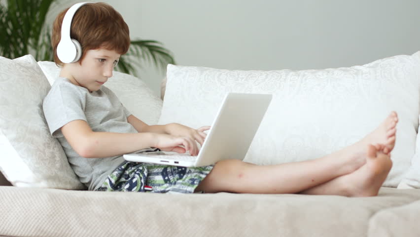 Funny little boy sitting on sofa with laptop expessing joy