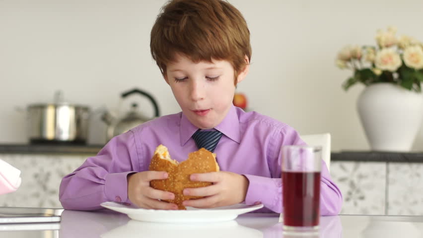 Little boy sitting at table eating burger and drinking juice