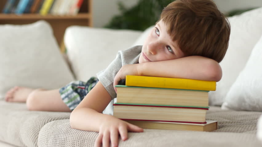Little boy lying on sofa with stack of books