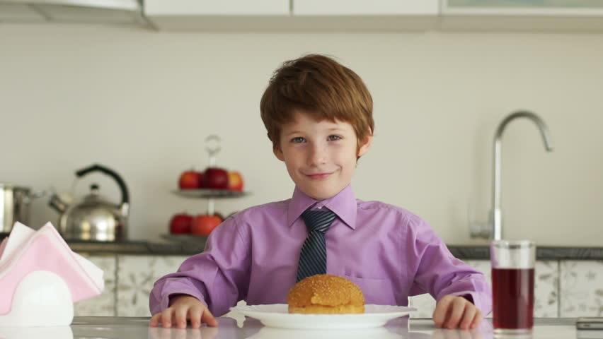 Little boy sitting at kitchen table and eating burger