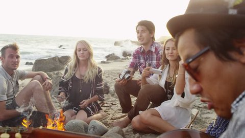 Group of young people hanging out at beach around campfire