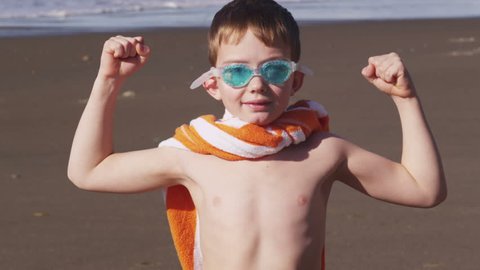 Young boy at beach flexing muscles with superhero costume