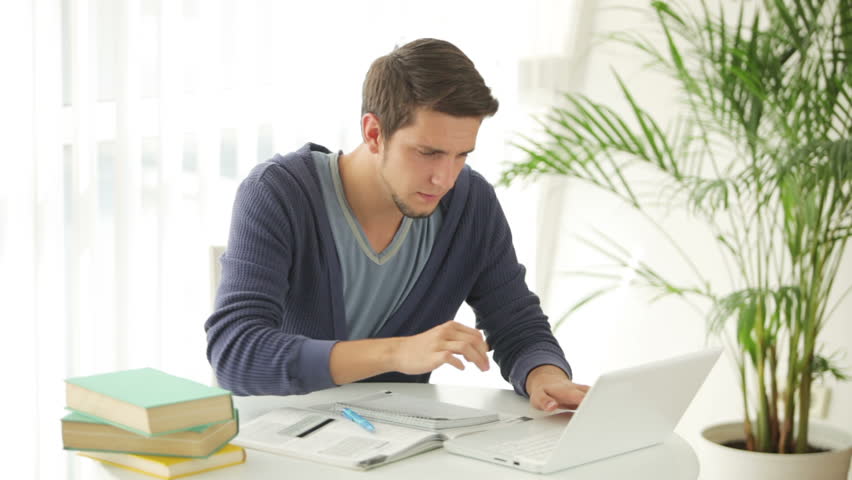 Charming young man sitting at table with laptop and credit card