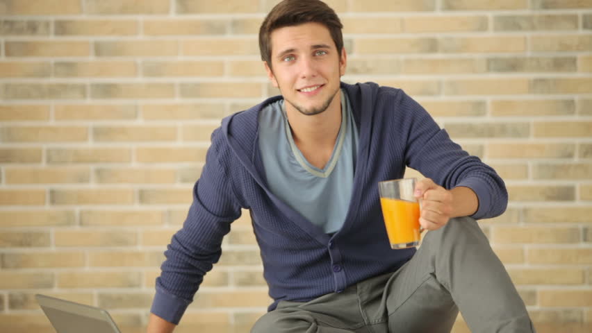 Good-looking guy sitting on floor using laptop and drinking juice
