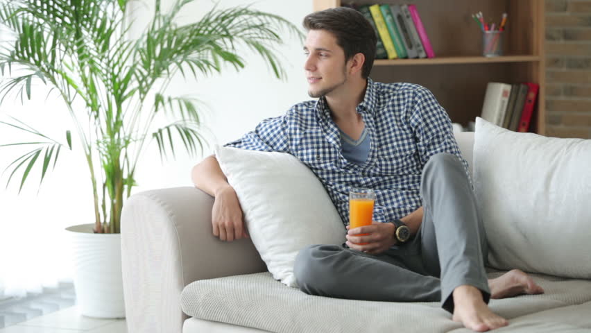 Good-looking guy sitting on sofa and drinking juice